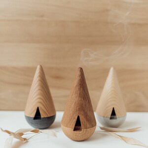 May include: Three wooden cone-shaped diffusers with a gray base. The middle diffuser is emitting a wisp of smoke.