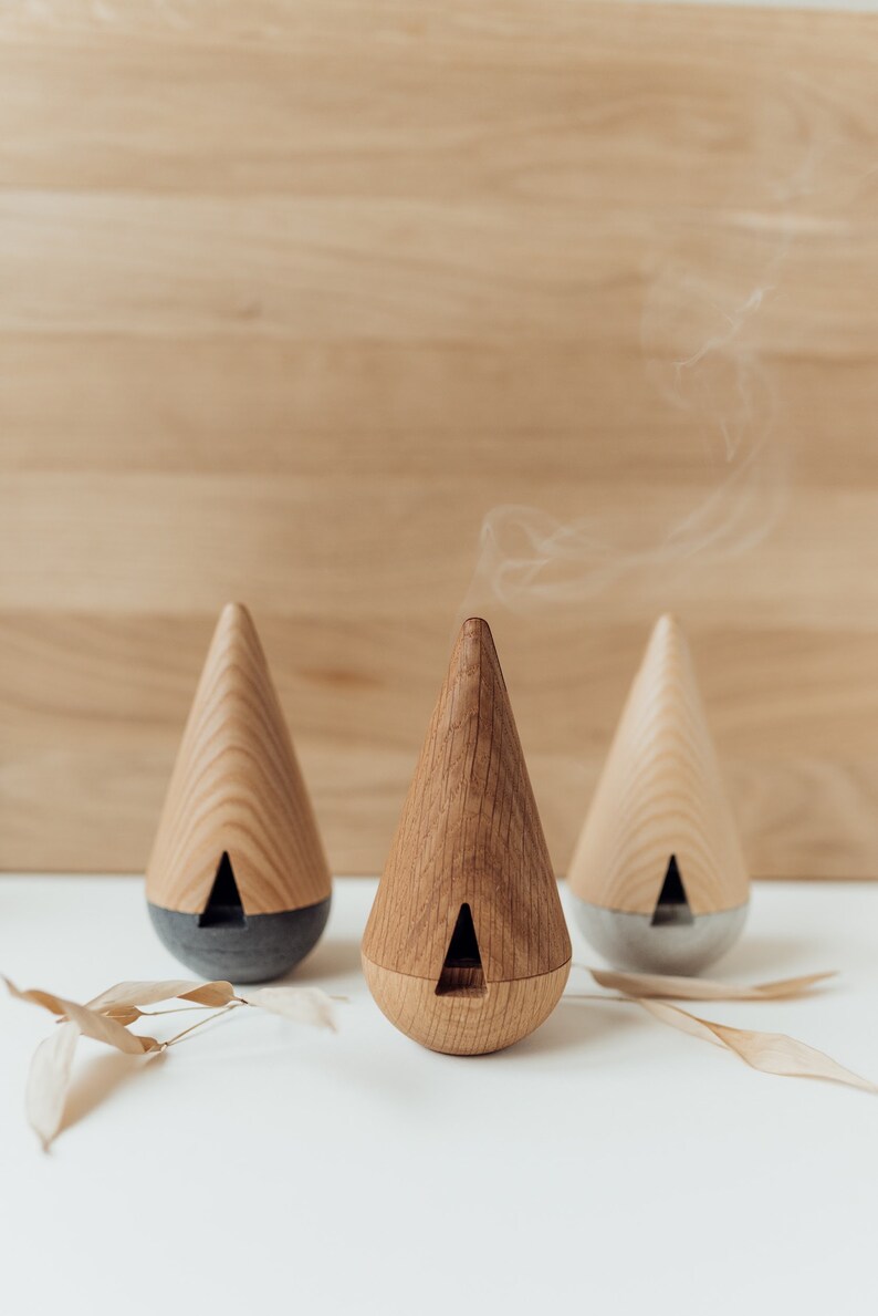 May include: Three wooden cone-shaped diffusers with a gray base. The middle diffuser is emitting a wisp of smoke.