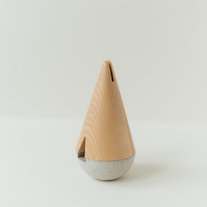 May include: A wooden and concrete spinning top in the shape of a cone. The top is light brown with a gray base.