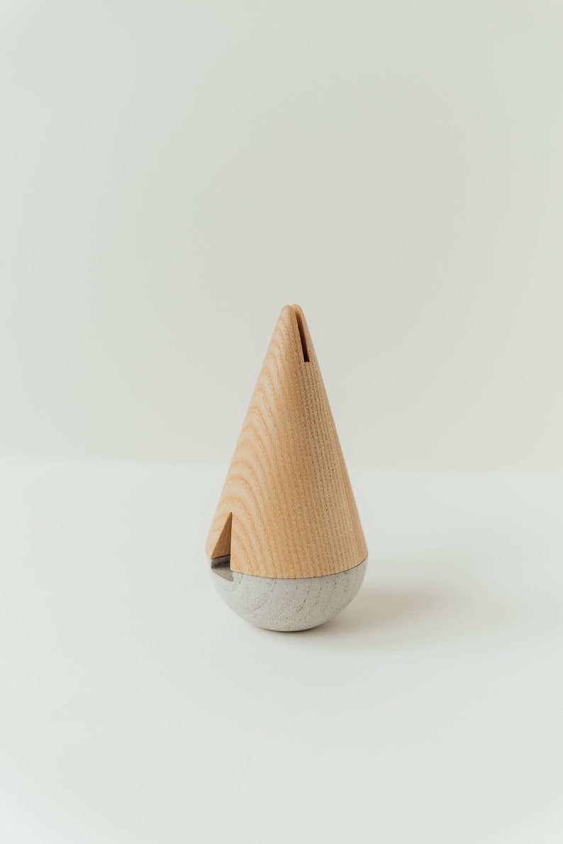 May include: A wooden and concrete spinning top in the shape of a cone. The top is light brown with a gray base.