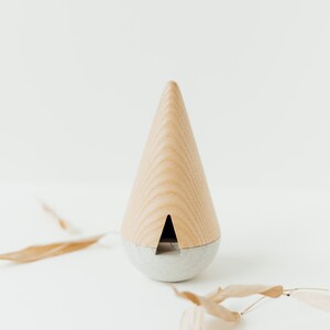 May include: A wooden cone-shaped incense burner with a gray base. The incense burner is on a white surface with dried leaves.