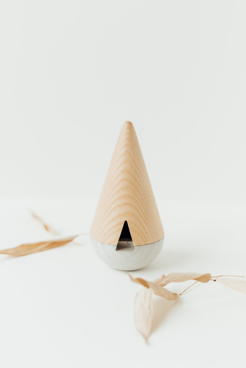 May include: A wooden cone-shaped incense burner with a gray base. The incense burner is on a white surface with dried leaves.