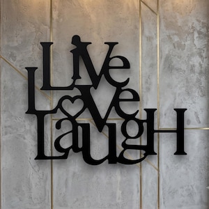 Könnte beinhalten: Ein Wandkunstobjekt aus schwarzem Metall mit den Wörtern LIVE, LOVE und LAUGH, die vertikal in einer fetten Serifenschrift gestapelt sind. Das Wort LOVE enthält eine Herzform, die in den Buchstaben O integriert ist und ein zusammenhängendes Design bildet.