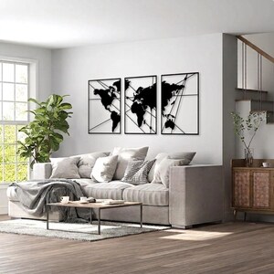 Peut inclure: Un ensemble de trois décorations murales en métal noir représentant une carte du monde. Chaque panneau rectangulaire affiche une partie des continents avec de fines lignes diagonales qui se croisent sur le cadre, créant un aspect géométrique.