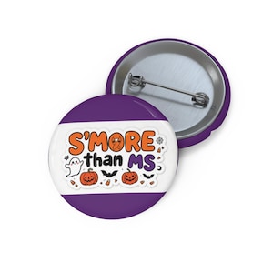 May include: A round purple pin-back button featuring the text S'MORE than MS in orange and black. The design includes a white ghost, two orange jack-o'-lanterns, black bats, candy corn, a spider web, and an orange awareness ribbon on a white background.