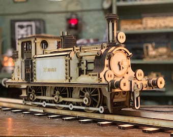 Può includere: Un motore di treno modello in legno con una base e ruote nere. Il motore è dipinto di bianco con accenti neri e la parola "VICTOR" stampata sul lato.