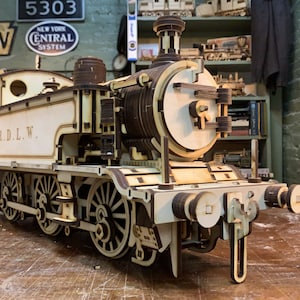 Puede incluir: Una locomotora de tren modelo de madera con un esquema de pintura blanco y marrón. La locomotora tiene una caldera grande y redonda y una cabina pequeña y abierta. La locomotora está etiquetada como "R.D.L.W."