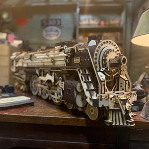 Puede incluir: Maqueta de madera detallada de una locomotora de vapor, con intrincados diseños recortados. El modelo es principalmente marrón y beige, con ruedas visibles, una chimenea y el número "5405". Se encuentra sobre una superficie de madera.