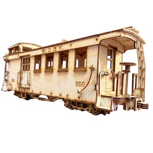 May include: A wooden model of a train car with the text "R. D. L. W." and "556" on the side. The car has windows and a door, and is made of light brown wood.