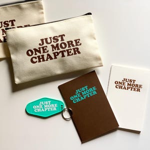 May include: A collection of items featuring the text "JUST ONE MORE CHAPTER". The items include two canvas zipper pouches, a brown notebook, a white notebook, and a teal keychain.