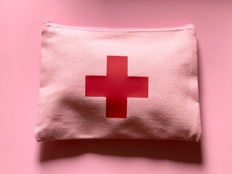 Pink pouch with a pink zipper and a red cross on the front.