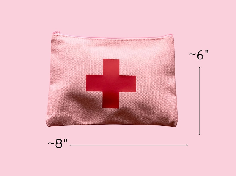 Puede incluir: Una bolsa con cremallera de lona rosa con una gran cruz roja en el centro. La bolsa mide aproximadamente 20 cm de ancho y 15 cm de alto. La bolsa de tem&aacute;tica m&eacute;dica est&aacute; dise&ntilde;ada para guardar suministros de primeros auxilios.
