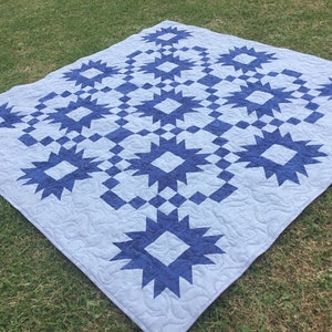 May include: A blue and white quilt with a starburst pattern. The quilt is made of cotton fabric and is quilted with a simple stitch.