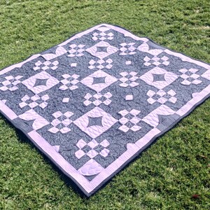 May include: A purple and gray quilt with a geometric pattern. The quilt is made of squares and diamonds, and it is quilted with a swirling design.