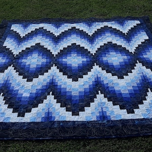 May include: A blue and white quilt with a geometric pattern. The quilt is made of squares and rectangles, and the pattern is a series of waves.