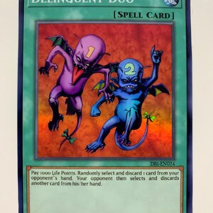 May include: A blue and purple "Delinquent Duo" trading card featuring two cartoon demons with the text "[SPELL CARD]" and "DB1-EN024".