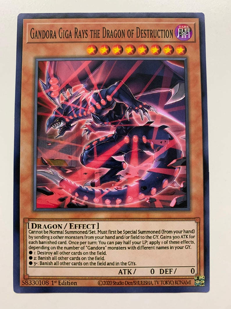 Peut inclure: Une carte de jeu de cartes &agrave; collectionner Yu-Gi-Oh! noire et rouge repr&eacute;sentant "Gandora Giga Rays the Dragon of Destruction". La carte repr&eacute;sente un dragon noir avec des yeux rouges et des faisceaux de lumi&egrave;re rouge &eacute;manant de son corps. Le texte de la carte d&eacute;crit l'effet d'invocation sp&eacute;ciale du dragon et ses pouvoirs puissants.