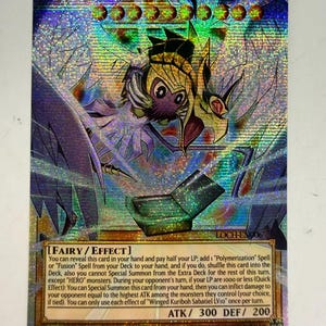 May include: A holographic trading card featuring "Winged Kuriboh Sabatiel LV10." The card has a colorful design with a winged creature and text. The card's ATK is 300, and DEF is 200. The card is a 1st Edition.