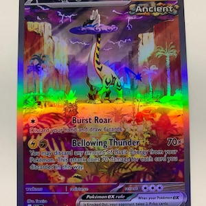 May include: A holographic Pokémon trading card featuring "Raging Bolt ex." The card showcases a long-necked creature with a cloud-like head, set against a backdrop of a purple sky and desert landscape. The card has a HP of 240 and includes text describing attack moves.