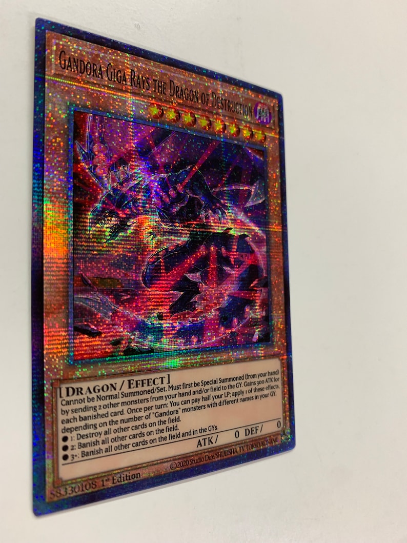 Peut inclure: Une carte de jeu de commerce holographique repr&eacute;sentant un dragon rouge, noir et bleu aux yeux brillants. La carte est intitul&eacute;e "Gandora Giga Rays the Dragon of Destruction" et porte le texte "DRAGON/EFFECT" dans le coin inf&eacute;rieur droit. La carte est issue du jeu de cartes &agrave; collectionner "Yu-Gi-Oh!"
