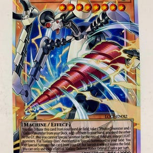 May include: A trading card featuring "GALAXY DEFENSE ROBOT ORBITAL 7". The card has a futuristic robot illustration with a red drill-like weapon. The card's background has blue and yellow energy effects. The card's text includes "MACHINE / EFFECT" and game instructions.