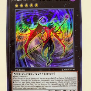 Puede incluir: Carta coleccionable holográfica con "Number C104: Umbral Horror Masquerade." La carta presenta una figura central con un bastón sobre un fondo oscuro. El texto incluye "Spellcaster/XYZ/Effect" y detalles del juego.