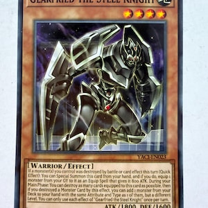Puede incluir: Una carta coleccionable de Yu-Gi-Oh! titulada Gearfried the Steel Knight, que muestra un guerrero con armadura negra y detalles rojos. La carta presenta el texto Warrior/Effect, ATK/1800, DEF/1600 y el código YAC1-EN023 en un borde marrón.