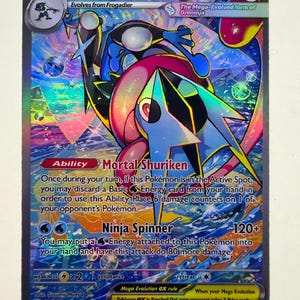 Op de afbeelding: Een Mega Greninja EX ruilkaart met een holografische, veelkleurige illustratie van het personage. De kaart toont 350 HP, de Mortal Shuriken-vaardigheid en de Ninja Spinner-aanval. De tekst bevat kaartdetails en spelregels.