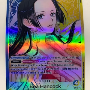 May include: A holographic trading card featuring Boa Hancock from the Seven Warlords of the Sea. The card has a colorful, iridescent background and displays the character's image with text detailing game mechanics. The card is labeled as a Leader card.