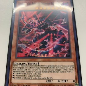 Peut inclure: Une carte de jeu de cartes &agrave; collectionner Yu-Gi-Oh! repr&eacute;sentant "Giga-Ray, le Dragon de la Destruction". La carte est rouge et noire et repr&eacute;sente un dragon rouge et noir avec des yeux rouges brillants. Le texte de la carte est le suivant : "Ne peut pas &ecirc;tre Invoqu&eacute; Normalement/Plac&eacute;. Doit d'abord &ecirc;tre Invoqu&eacute; Sp&eacute;cialement (depuis votre main) en envoyant 2 autres monstres de votre main et/ou du terrain au Cimeti&egrave;re. Gagne 300 ATK pour chaque carte bannie. Une fois par tour : Vous pouvez payer la moiti&eacute; de vos PV ; appliquez 1 de ces effets, en fonction du nombre de monstres "Gandora" avec des noms diff&eacute;rents dans votre Cimeti&egrave;re. 1 : D&eacute;truisez toutes les autres cartes sur le terrain. 2 : Bannissez toutes les autres cartes sur le terrain. 3 : Bannissez toutes les autres cartes sur le terrain et dans les Cimeti&egrave;res."