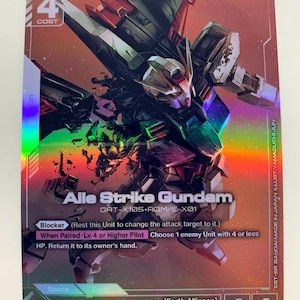 Puede incluir: Una tarjeta coleccionable con el Alle Strike Gundam, un robot mecha con un esquema de color rojo, blanco y negro. La tarjeta tiene un acabado holográfico e incluye texto como "Blocker" y "Kira Yamato".
