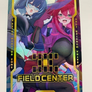 Peut inclure: Une carte à collectionner holographique avec deux personnages de style anime vêtus en sorcières. La carte a des accents dorés et le texte "EXTRA MONSTER ZONE" et "FIELD CENTER". Les personnages sont dans des tons de violet, rose et bleu.