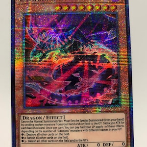 Peut inclure: Une carte de jeu de collection repr&eacute;sentant un dragon noir et violet fonc&eacute; avec des yeux rouges. La carte est intitul&eacute;e "Gandora Giga Rays the Dragon of Destruction" et est une carte "DRAGON/EFFET" de type "T&Eacute;N&Egrave;BRES". La carte a un fond noir avec un effet holographique.