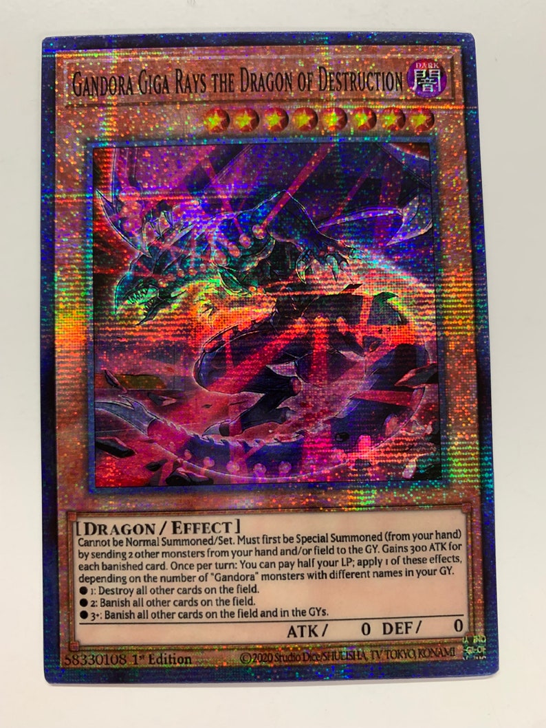 Peut inclure: Une carte de jeu de collection repr&eacute;sentant un dragon noir et violet fonc&eacute; avec des yeux rouges. La carte est intitul&eacute;e "Gandora Giga Rays the Dragon of Destruction" et est une carte "DRAGON/EFFET" de type "T&Eacute;N&Egrave;BRES". La carte a un fond noir avec un effet holographique.