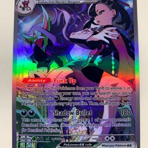 Puede incluir: Carta Pokémon holográfica de Marnie's Grimmsnarl EX. La tarjeta muestra una colorida ilustración de un personaje con ropa oscura y una criatura verde y morada. El texto describe habilidades y ataques, con 320 PS.