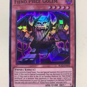 Puede incluir: Carta coleccionable de Fiend Piece Golem con un esquema de color púrpura oscuro y azul. La carta presenta un monstruo con rostro de calavera, brazos encadenados y cuerpo en bloques. El texto incluye el nombre, atributos y efectos del monstruo.