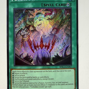 Puede incluir: Carta de hechizo Forbidden Crown holográfica con borde verde. La carta presenta el texto "Forbidden Crown" y una ilustración detallada de una figura espectral y una corona. Los efectos de la carta se enumeran a continuación.