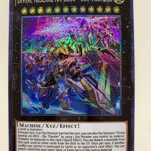 May include: A trading card for the "Divine Arsenal AA-ZEUS - Sky Thunder" monster from the Yu-Gi-Oh! Trading Card Game. The card is a Machine/XYZ/Effect monster with an attack and defence power of 3000. The card is a light blue and white colour with a purple and blue background.