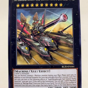 May include: A trading card depicting a Superdreadnought Rail Cannon Flying Launcher. The card has a black background with the card name and attributes at the top. The card text describes the card's effects. ATK/3800 DEF/3000. The card is from the Machine/XYZ/Effect series.