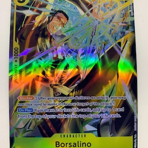 Pode incluir: Um cartão colecionável holográfico com o personagem Borsalino de Egghead/Navy. O cartão tem uma borda verde e amarela com o número 5 e o texto "COUNTER +1000". O cartão também tem o texto "Blocker" e "On Play".