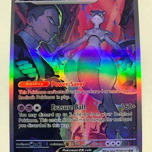 Puede incluir: Una carta coleccionable Pokémon holográfica con Mewtwo ex. La carta tiene un esquema de color púrpura y arcoíris con el texto "Team Rocket's Mewtwo ex" y "Power Saver". La carta también presenta una ilustración de personaje e instrucciones del juego.
