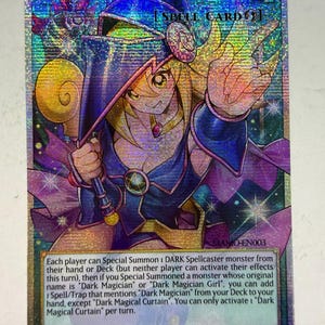 Può includere: Una carta collezionabile olografica intitolata Dark Magical Curtain, una carta magia che raffigura un personaggio biondo con cappello e abito da mago blu. La carta mostra istruzioni di gioco, il codice MAMO-EN003 e una finitura olografica.