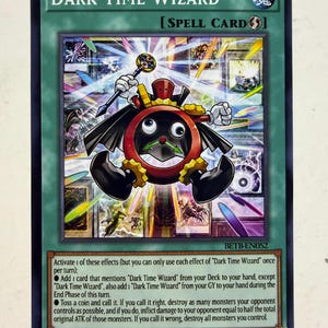 May include: A Dark Time Wizard Yu-Gi-Oh! spell card featuring a central clock-like character with a red frame, black face, and green hands, holding a staff. The background displays various card illustrations with light streaks and text.