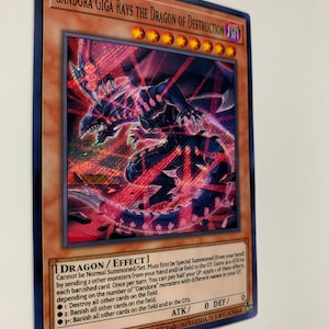 Peut inclure: Une carte &agrave; jouer "Gandora Giga Rays the Dragon of Destruction" rouge et noire repr&eacute;sentant un dragon aux yeux rouges et au corps noir. La carte est du jeu de cartes &agrave; jouer "Yu-Gi-Oh!"