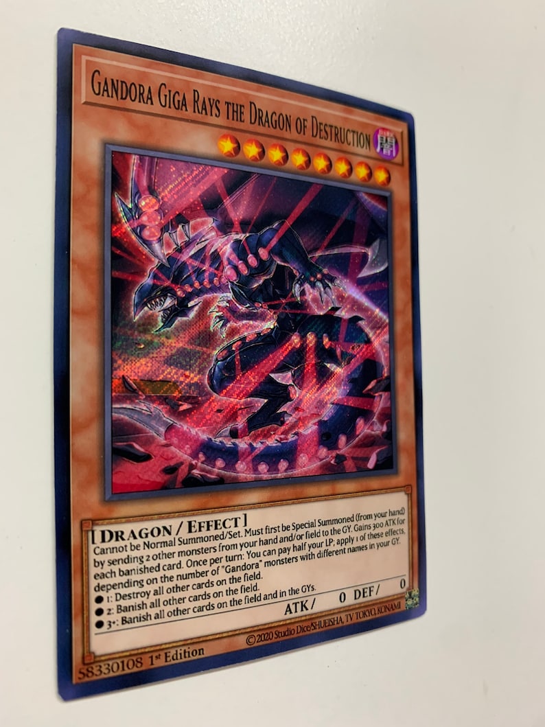 Peut inclure: Une carte &agrave; jouer "Gandora Giga Rays the Dragon of Destruction" rouge et noire repr&eacute;sentant un dragon aux yeux rouges et au corps noir. La carte est du jeu de cartes &agrave; jouer "Yu-Gi-Oh!"