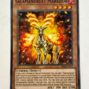 May include: A Yu-Gi-Oh! trading card titled Salamangreat Markhor, a level 4 FIRE attribute Cyberse effect monster. The card features a golden, mechanical goat-like creature surrounded by flames, with 300 ATK and 2100 DEF stats printed below.