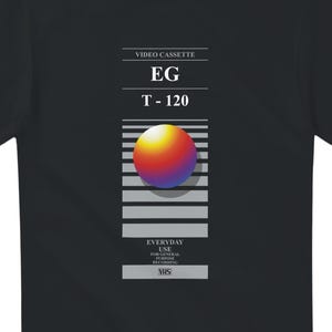 May include: Black t-shirt with a retro VHS tape design. The graphic includes the text "VIDEO CASSETTE", "EG", "T-120", and "EVERYDAY USE". A colourful sphere is centered on the tape design.