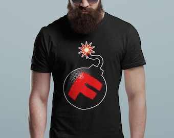 Pode incluir: Camiseta preta com um gráfico de bomba. A bomba tem um "F" vermelho dentro de um contorno branco e um pavio de estrela vermelha. A camiseta é de gola redonda.