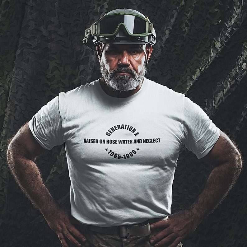 May include: A white t-shirt with the text "GENERATION X RAISED ON HOSE WATER AND NEGLECT *1965-1980*". The person in the image is wearing a military-style helmet with goggles. The background has a camouflage pattern.
