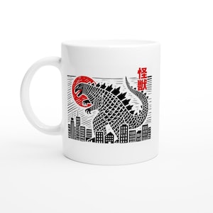 May include: White ceramic mug featuring a black and white illustration of Godzilla standing in a city with a red sun in the background. The Japanese text "怪獣" is printed on the mug.